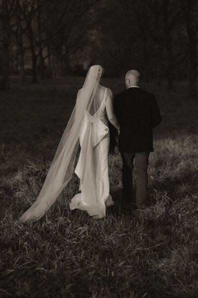 An editorial and aesthetic black and white wedding photo of a bride and groom in Coffs Harbour walking into a patch of light in a country orchard