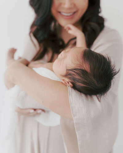 Mother holding newborn against neutral backdrop, Bay Area newborn photographer session.