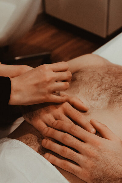 Female acupuncturist inserts needle into male patient's hand as he lays shirtless on acupuncture table.