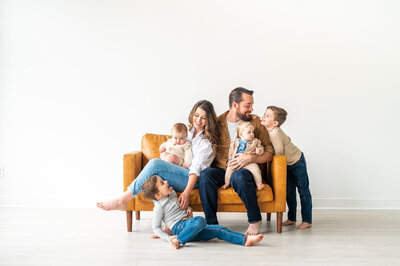 Reg and Kala with their 4 kids, all smiling at each other, sitting on a large caramel chair. No one is looking at the camera, it is a candid moment.