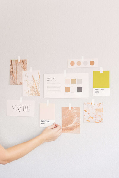 Hand holding pink Pantone swatch to wall with other pieces of paper to create a mood board