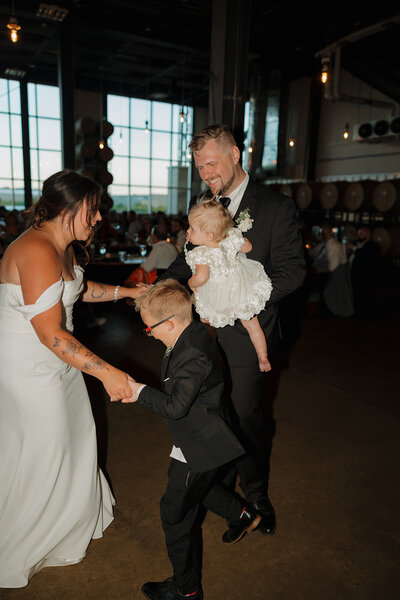 bride and groom dance with their kids on the dance floor at their wedding reception in mount horeb, wisconsin