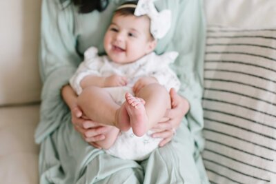 6 month old baby sitting on mother and smiling  with toes in the air