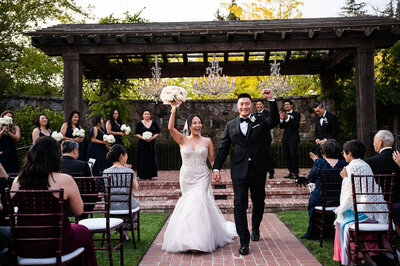 Bride and groom first kiss during wedding ceremony under wooden pergola at Estate Yountville with wedding party and guests, San Francisco Bay Area wedding photography