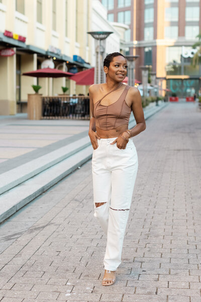 Woman walking down the street in the Bay Area looking to the side and smiling with her hands in her pocket posing for her brand photoshoot.