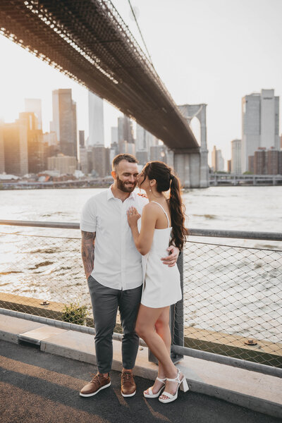 man and woman embracing in front of water with city in the background