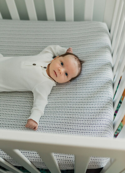 Baby photography photoshoot with newborn in a crib wearing a white onesie.