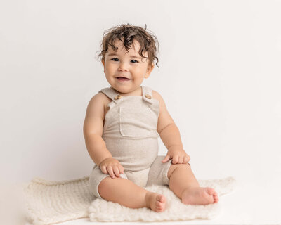 baby boy in cream overalls smiling in portland photography studio