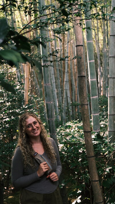 Portrait of Natalie Dyer, founder of Natalie Dyer Photo, standing in a serene bamboo forest in Kyoto, Japan, capturing a moment of calm and natural beauty..