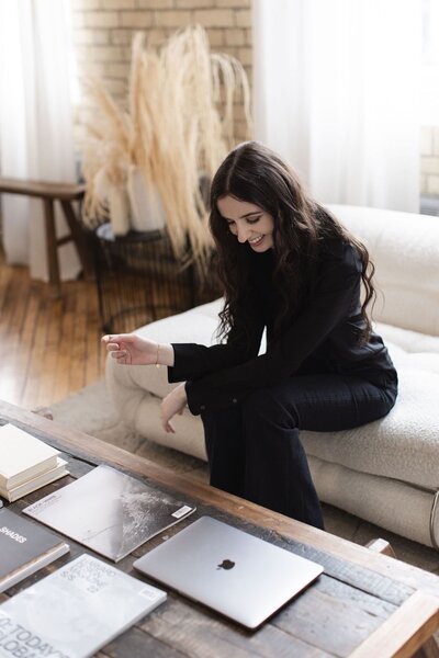 Brand photo of woman sitting on a white couch next to laptop and magazine on coffee table