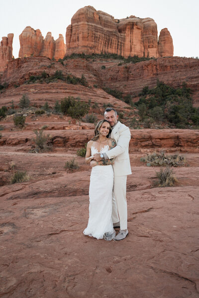 Bride and groom embrace during their intimate elopement at Cathedral Rock in Sedona, Arizona, with stunning red rock formations towering behind them.