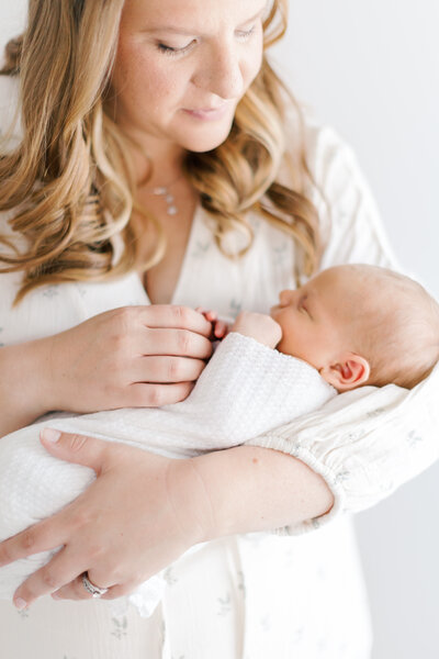 A mother snuggles her newborn baby in a sunlit nursery during her NJ newborn photos.