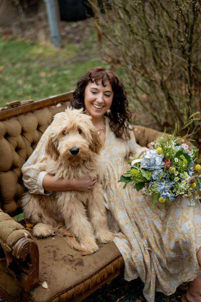 Pittsburgh wedding florist Heavenly Blooms sitting on a couch outdoors holding a dog and a bouquet 
