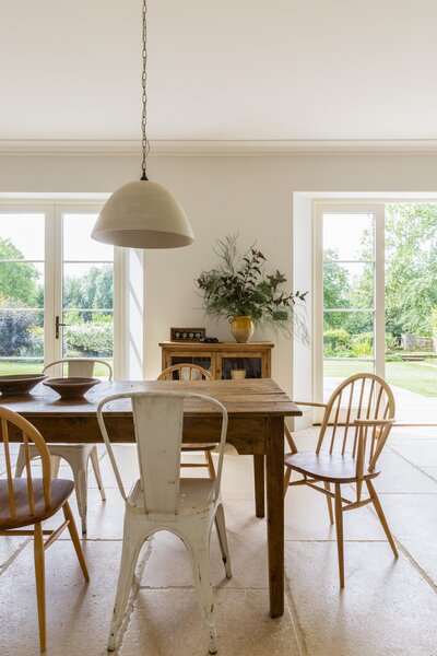 Wooden dining chairs underneath hanging light surrounded by garden