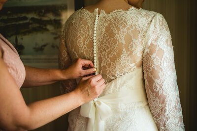 The back of a brides lacy, vintage wedding dress being buttoned by her mother.
