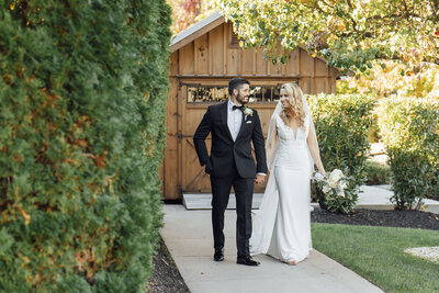 The Hamilton Manor | Bride and groom walking hand in hand with barn in background during summer wedding photo | Hamilton Township, New Jersey