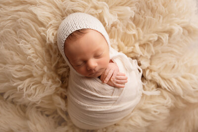 newborn boy cream wrap on fur with hat