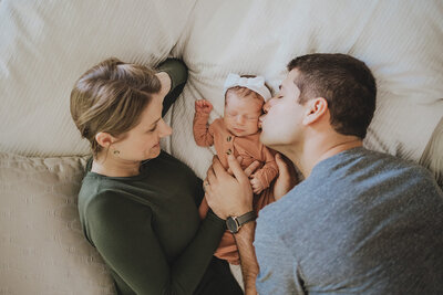 Woman and Man lying on bed with newborn in mauve onesie with white bow in Washington DC