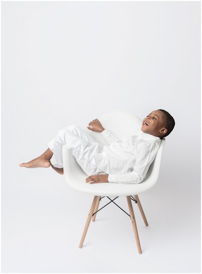 Boy laying across white and smiling  chair during portrait session