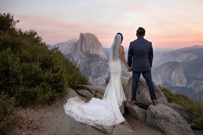 A newlywed couple stands hand in hand, gazing at Half Dome during their Yosemite elopement at sunset. Captured by Yosemite elopement photographers, this intimate moment reflects the beauty and adventure of a wedding in the mountains.