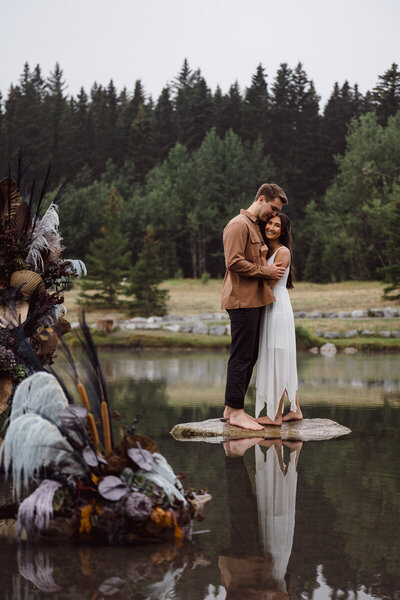 A couple standing on a rock in a pond during their Banff engagement session.