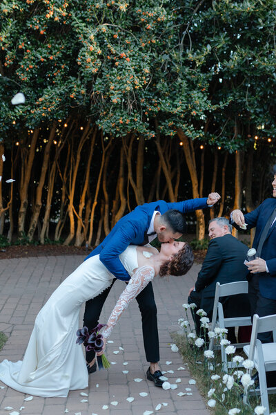 Bride and groom share a kiss during their outdoor wedding ceremony in North Carolina, beautifully captured under twinkling lights by Hallie Noel Photography