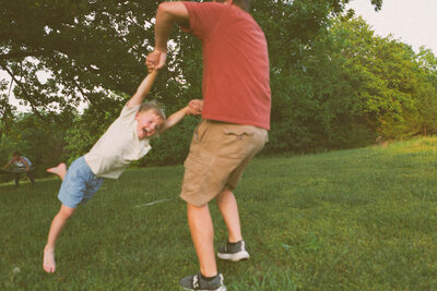 son is swung by dad during summer family session in green field