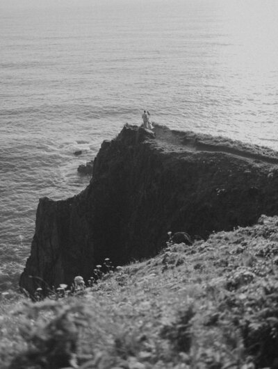 A couple stand on a cliff overlooking the Oregon Coast