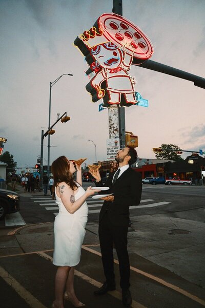 Elopement couple sharing a slice of pizza in front of the iconic Home Slice Pizza sign on South Congress in Austin, Texas. The bride is in a white dress and the groom in a black suit, capturing a fun and candid moment during their downtown celebration.