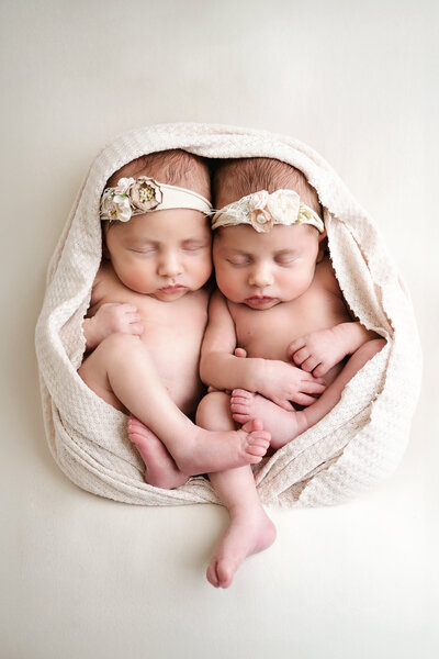 This heartwarming twin newborn photo showcases two beautiful babies wrapped in soft beige fabric and adorned with delicate floral headbands. Captured in a professional photography session in Pittsburgh, this image perfectly reflects the sweetness and connection of newborn twins.