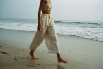 Editorial photo of a woman walking along the beach in neutral linen clothing, symbolizing freedom, flow, and intentional design at Kathalyst Design Studio.