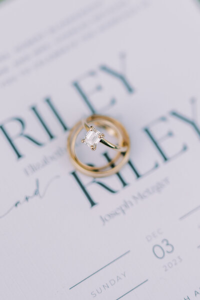 Close up image of wedding rings sitting on top of a wedding invitation
