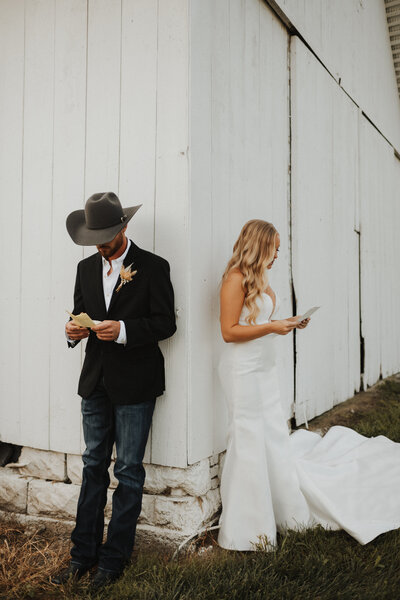 bride and groom reading letters from each other next to a white barn