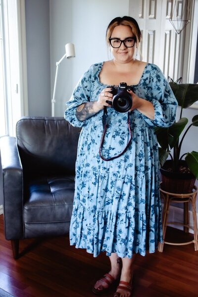 Woman in a blue floral, flowy dress holding a professional camera.