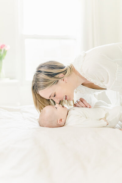 Mother leans in with a smile while her baby looks up at her during a light-filled Kansas City in-home newborn session
