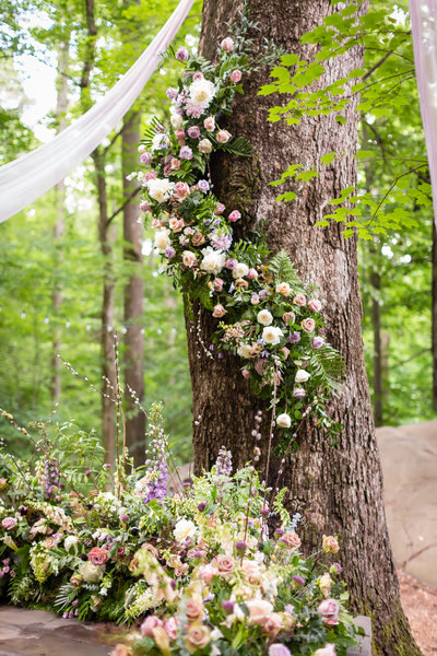 Silk chiffon and floral garland draped tree in outdoor forest wedding ceremony