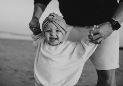 Baby smiling holding dad's hands walking in black and white image