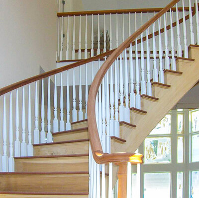 Custom curved wood staircase with white spindles completed for a home renovation project in Muttontown.