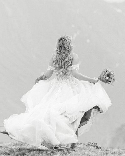 This dramatic portrait captures the bride walking away toward the towering mountains after her helicopter wedding ceremony. The vast and powerful mountain backdrop creates a stunning and awe-inspiring scene, highlighting the adventure and elegance of her special day.