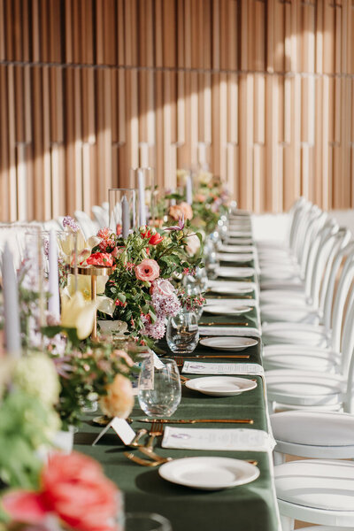 A bride and groom stand in the middle of the O'Born Room at the National Arts Centre for their wedding, featuring a beautiful white dress and white and black tuxedo, surrounded by black guest tables and luxurious white and gold leather chairs with white floral centrepieces in the glass room.
