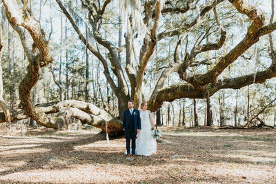 Groom in blue suit with brown hair holding hands with bride in white lace dress at the Island House by Charleston wedding photographer, Stephanie Bailey Photography