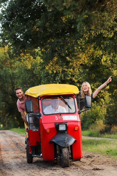 Twee mensen poseren bij een rode TukTuk tijdens een tocht door Twente.