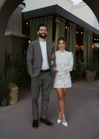 A stunning outdoor wedding ceremony in Scottsdale, Arizona, with a breathtaking mountain backdrop. Guests in vibrant pink dresses watch as the bride and groom exchange vows under a floral arch at sunset.