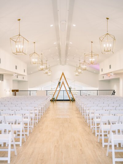 Photo of indoor ceremony space set up with chairs and ceremony arch