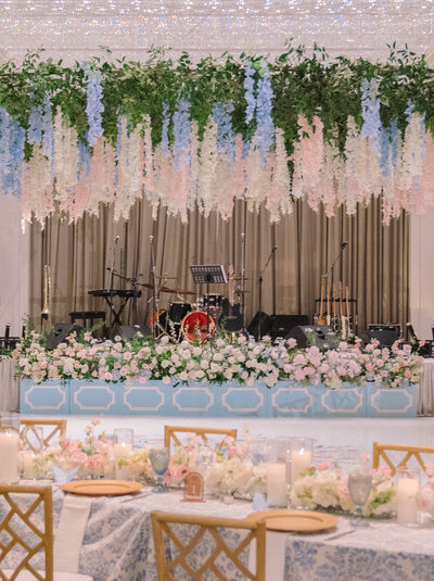 A colorful hanging installation overtop of a floral runner and candle lit table