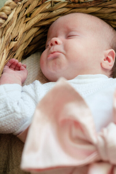Newborn baby girl lays in a basket while pouting her lips in her sleep