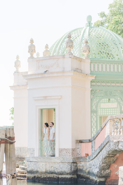 An engagend couple walking away from the camera, the bride is looking back at the camera, the set up is the beautiful garden of the Vizcaya Museum