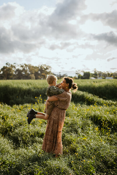 Mother and son embrace playfully among tall grass and yellow blossoms