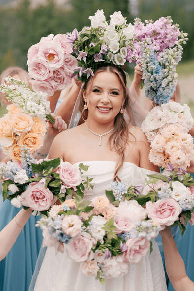 Smiling bride surrounded by pastel floral bouquets on her wedding day.
