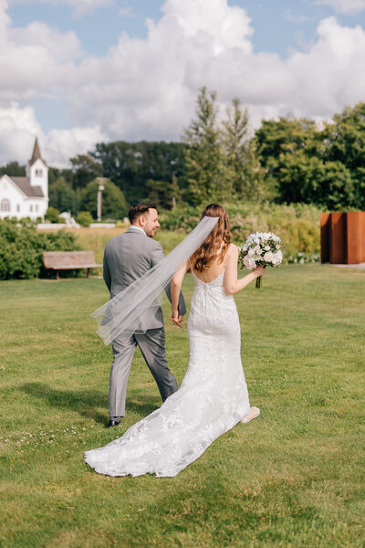 Bride and groom holding hands walking through a field at sunset